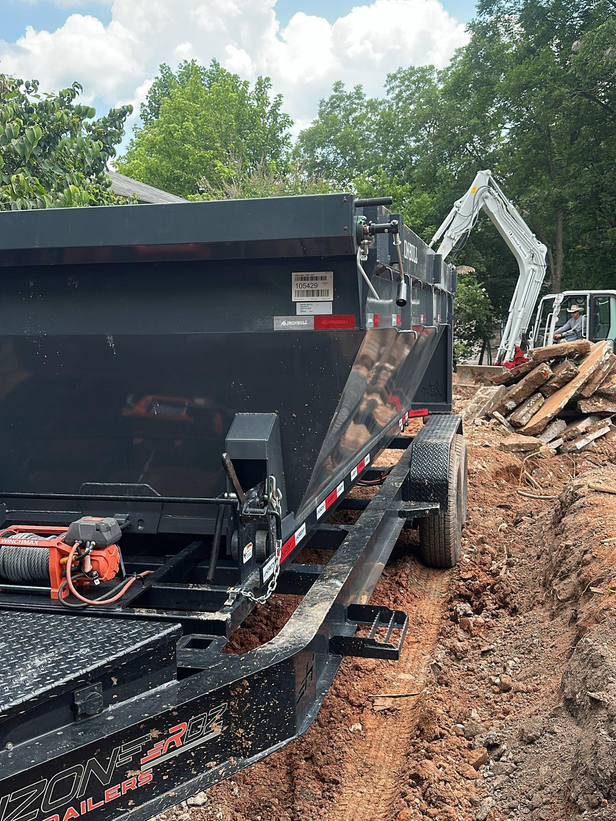 Black dumpster trailer beside demolition debris and compact equipment