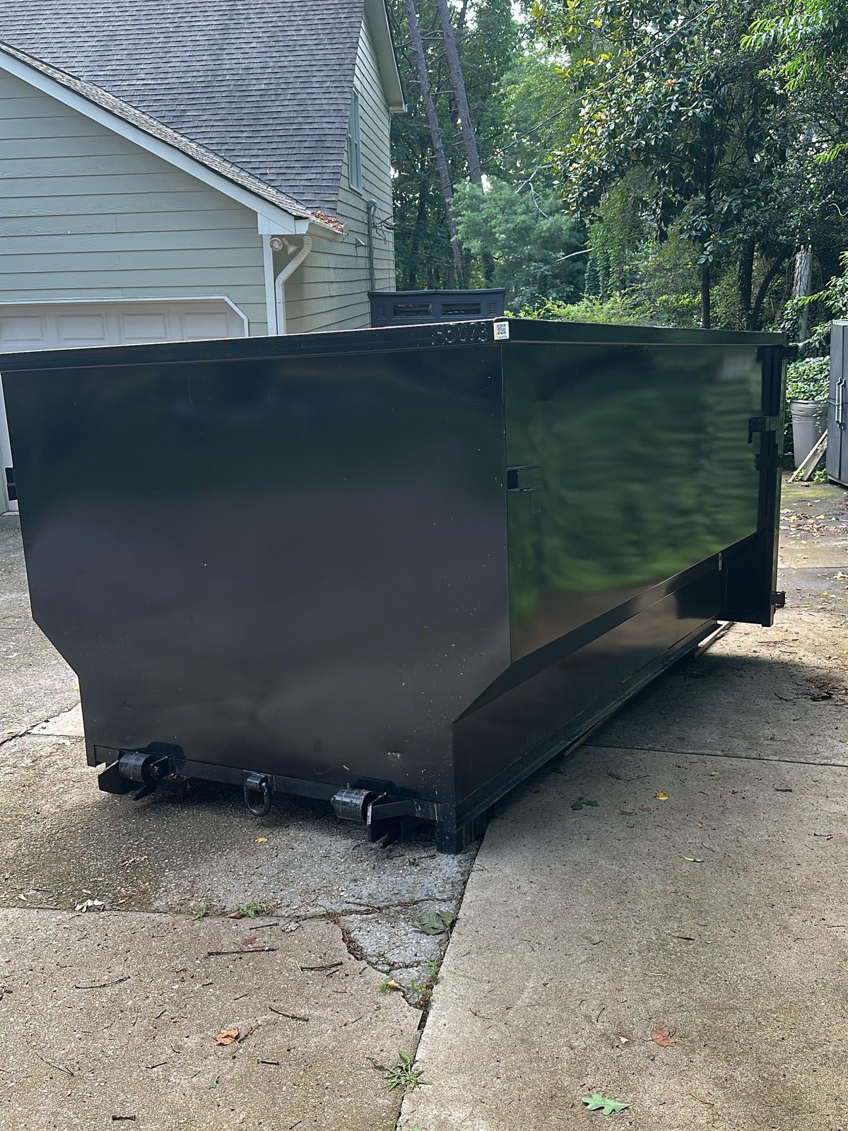 Black dumpster positioned neatly in a residential driveway