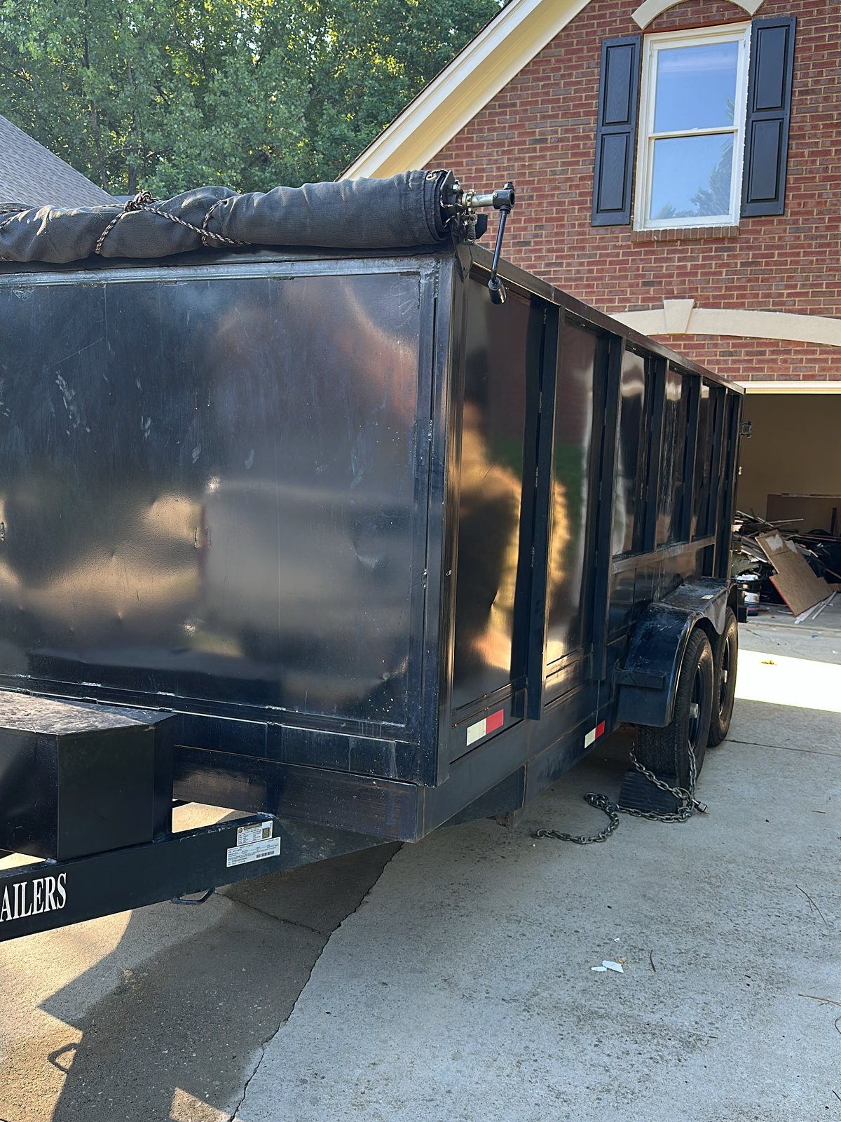 Black roll-off dumpster placed beside a brick home driveway
